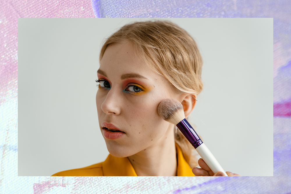 Montagem em fundo lilás e rosa claro com foto de garota passando pincel de maquiagem no rosto