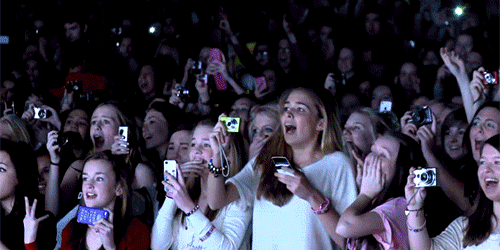 Adolescentes gritam na plateia do show e apostam suas câmeras para o palco