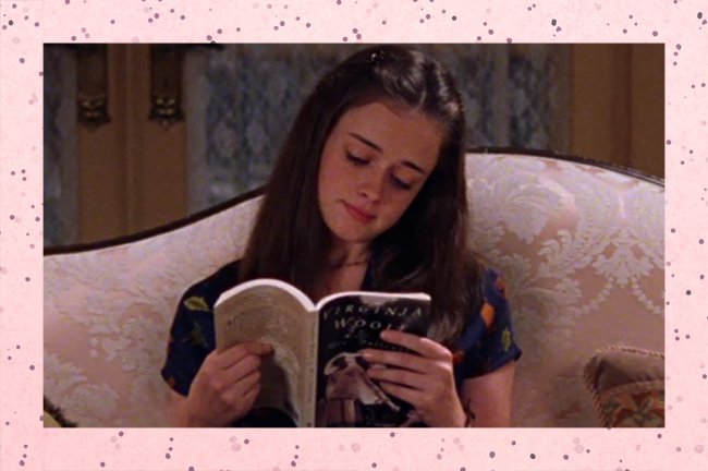 Foto de uma menina branca, de cabelos castanho, lendo um livro sentada no sofá