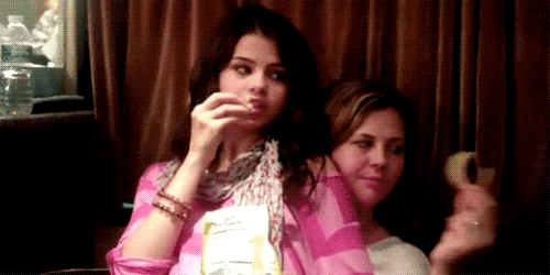 Selena Gomez comendo um salgadinho Cheetos no colo da amiga