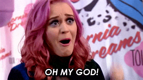 Katy Perry supresa com cabelo rosa e as mãos perto do rosto.