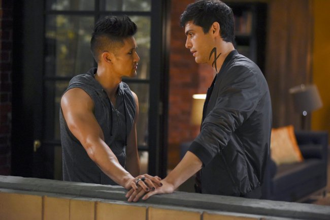 Magnus e Alec na série Shadowhunters; eles estão com roupas pretas se encarando com as mãos uma por cima da outra