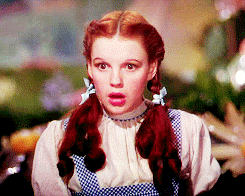 Gif da Dorothy, de O Mágico de Oz, com expressão facial surpresa, boca aberta e levando a mão perto da boca.