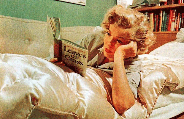 Marilyn Monroe aparece deitada e segurando um livro