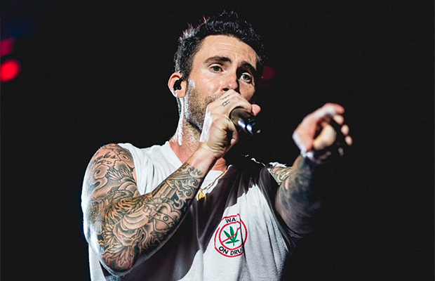 Vocalista do Maroon 5 cantando com microfone próximo ao rosto enquanto estende a outra mão para o público