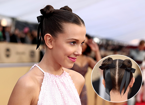 Millie Bobby Brown posando para foto usando coque elaborado e vestido branco.