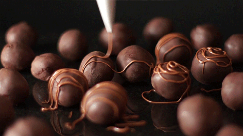Gif mostra trufas de chocolate sendo cobertas por delicados fios de chocolate saindo de um saco de confeiteiro.