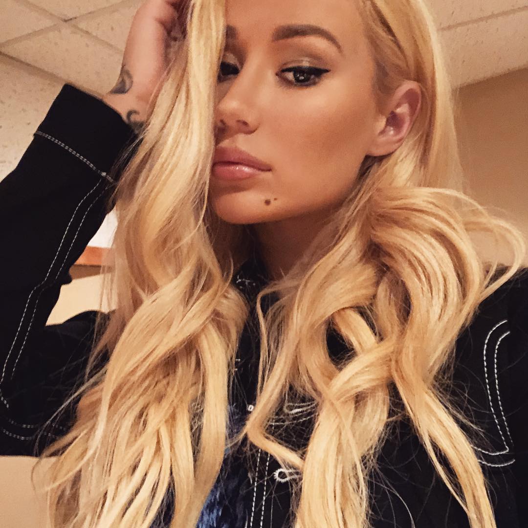 Selfie de Iggy Azalea com a mão no cabelo e a franja escondendo parte de seu rosto; a expressão da cantora é mais séria e ela usa uma blusa preta