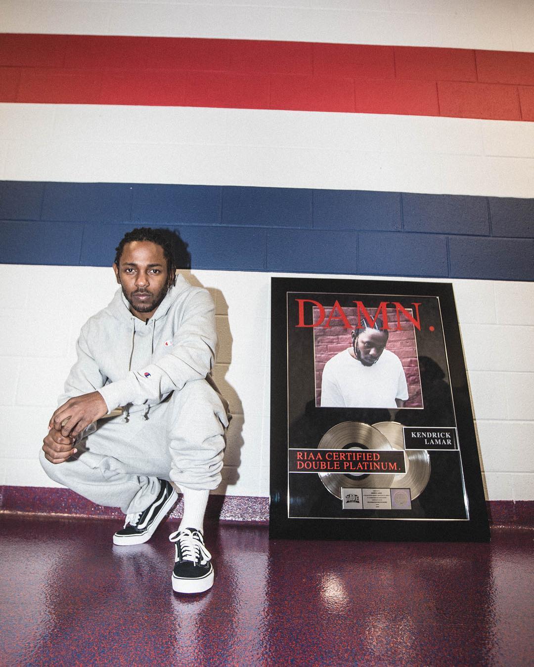 Kendrick Lamar posando ajoelhado para foto ao lado de placa de cerificado de seu álbum DAMN