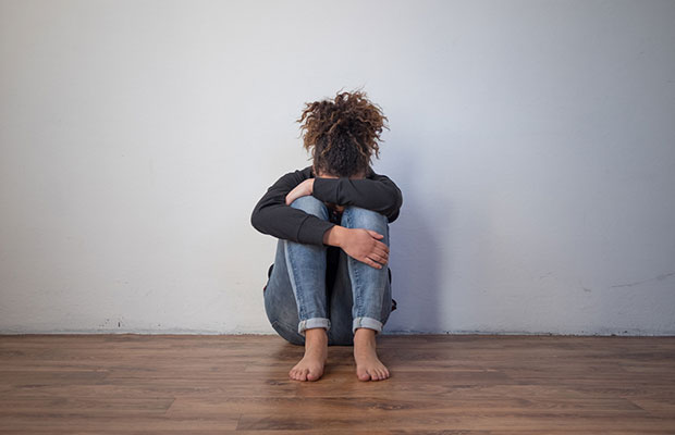 Foto de uma menina negra chorando e escondendo o rosto, sentada no chão