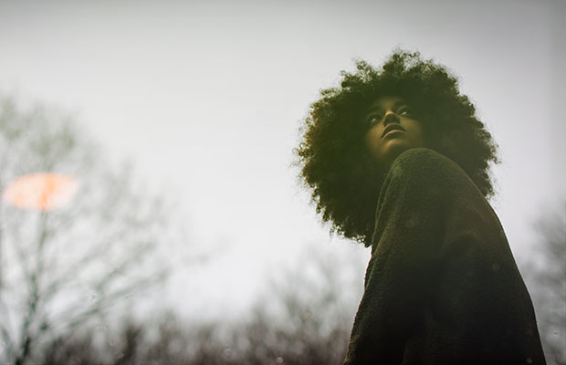 Foto de uma menina negra, com cabelo black power e agasalho preto, olhando para cima