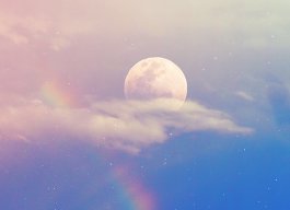 céu azulado com um arco íris. Atrás de uma das nuvens está uma lua cheia parcialmente coberta