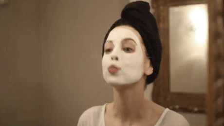 Gif da influenciadora Zoella com máscara facial branca mandando beijo na frente do espelho e com toalha no cabelo enquanto faz sua rotina de skincare
