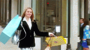 Gif da Cher, do filme As Patricinhas de Beverly Hills, fazendo compras. Ela está segurando sacolas nas duas mãos, sorrindo e andando.
