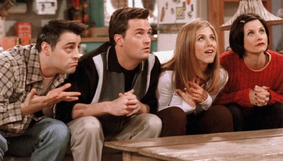 Foto com quatro dos seis protagonistas de Friends; em ordem da esquerda para direita sentados no sofá estão Joey, Chandler, Rachel e Monica olhando para frente inclinados com uma postura e expressão de expectativa, como se fossem ouvir uma história ou um segredo