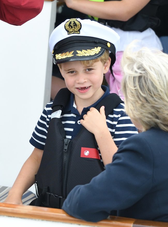 Prince George sorrindo e vestindo roupa que lembra estilo marinheiro e chapéu de marinheiro no evento esportivo King's Cup Regatta;