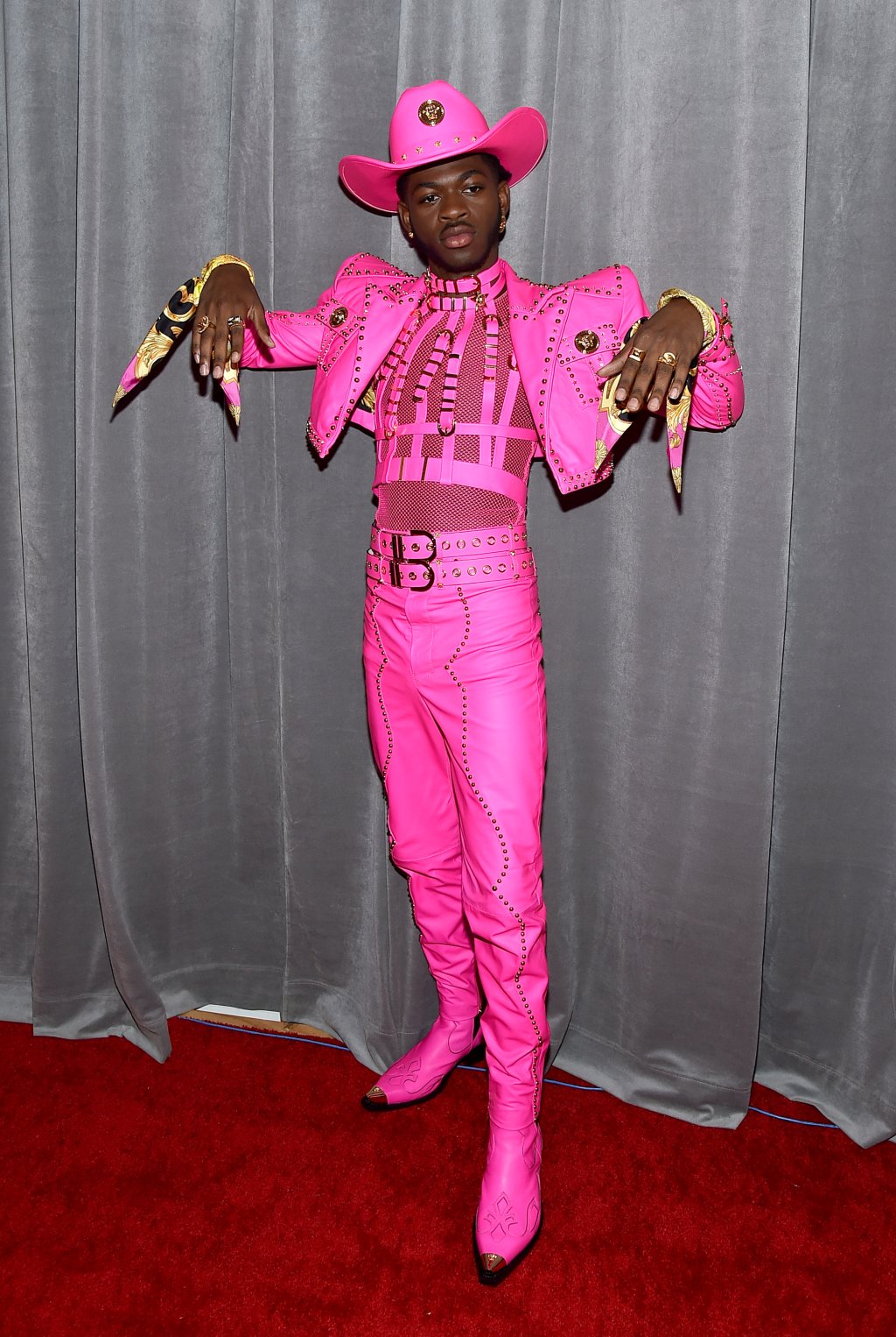 Lil Nas X no red carpet do GRAMMY Awards 2020 com terno e chapéu cor-de-rosa e com expressão séria exibindo as mãos