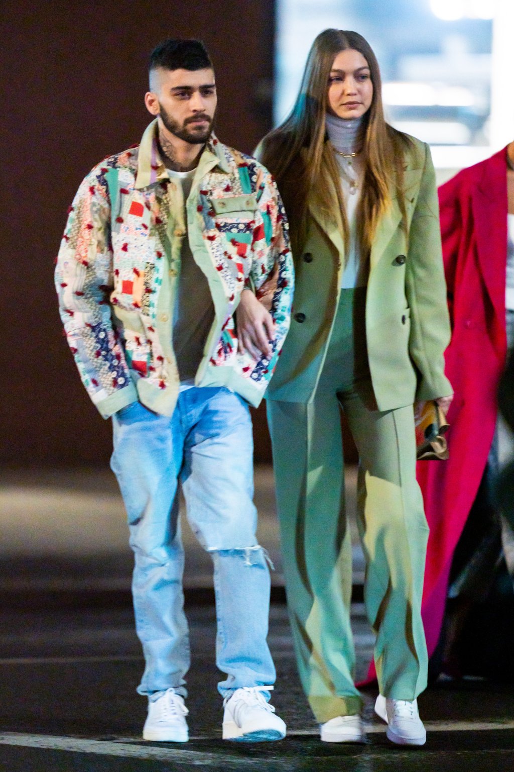 Zayn Malik e Gigi Hadid fotografados em Nova York; o cantor está de calça jeans de lavagem clara e um casaco branco com detalhes coloridos enquanto a modelo usa um look de alfaiataria na cor verde; ambos estõ com expressão séria e Gigi está de braço dado com o cantor
