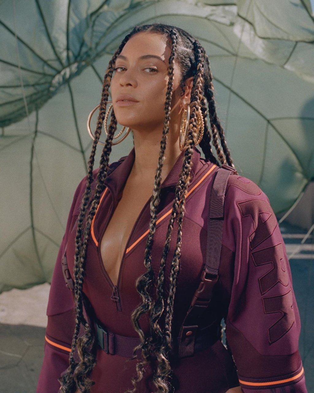 Beyoncé usando um casaco vinho com detalhes em laranja e brinco de argolas. Ela está com a cabeça levemente inclinada para trás e com expressão facial séria.