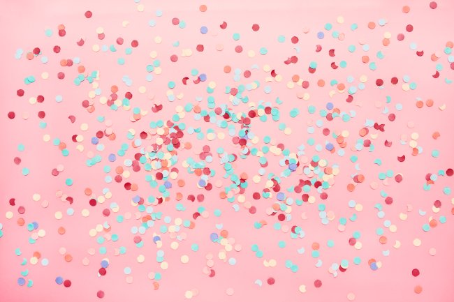 Confetes coloridos de papel sobre uma mesa rosa