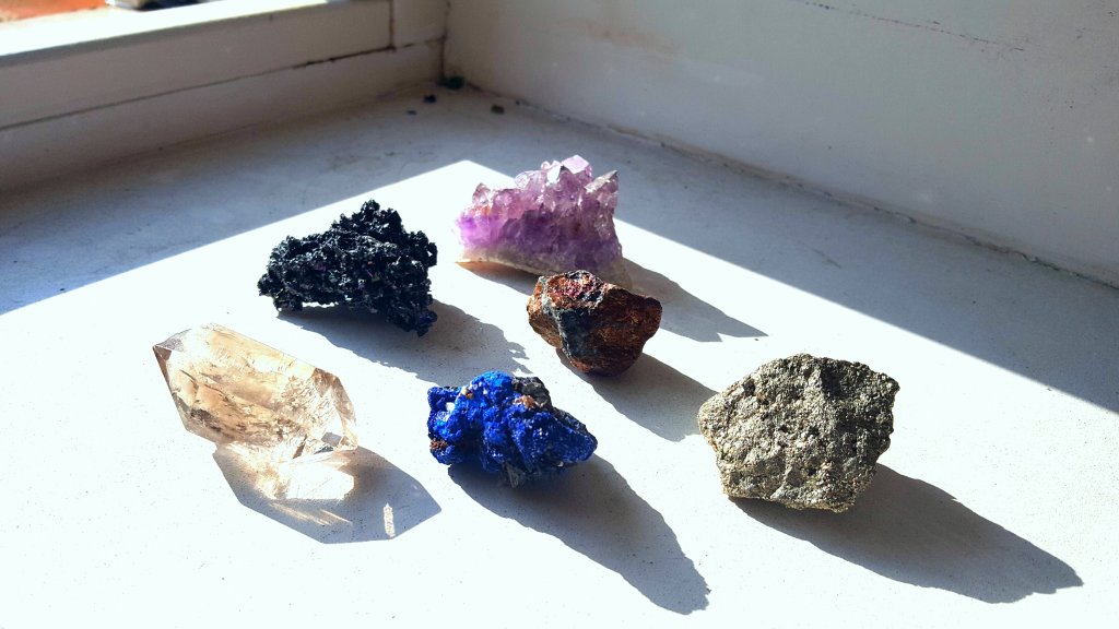 Pedras e cristais em cima de uma mesa branca com a luz da janela refletindo neles