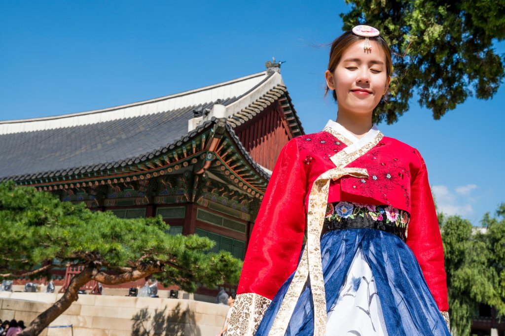 Menina usando trajes típicos da cultura da Coreia do Sul. Atrás dela há um templo