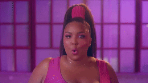 Lizzo, no clipe de Juice, usando body rosa e cabelo preso em um rabo com scrunchie rosa. Ela está apontado para a câmera com o dedo e falando "You"