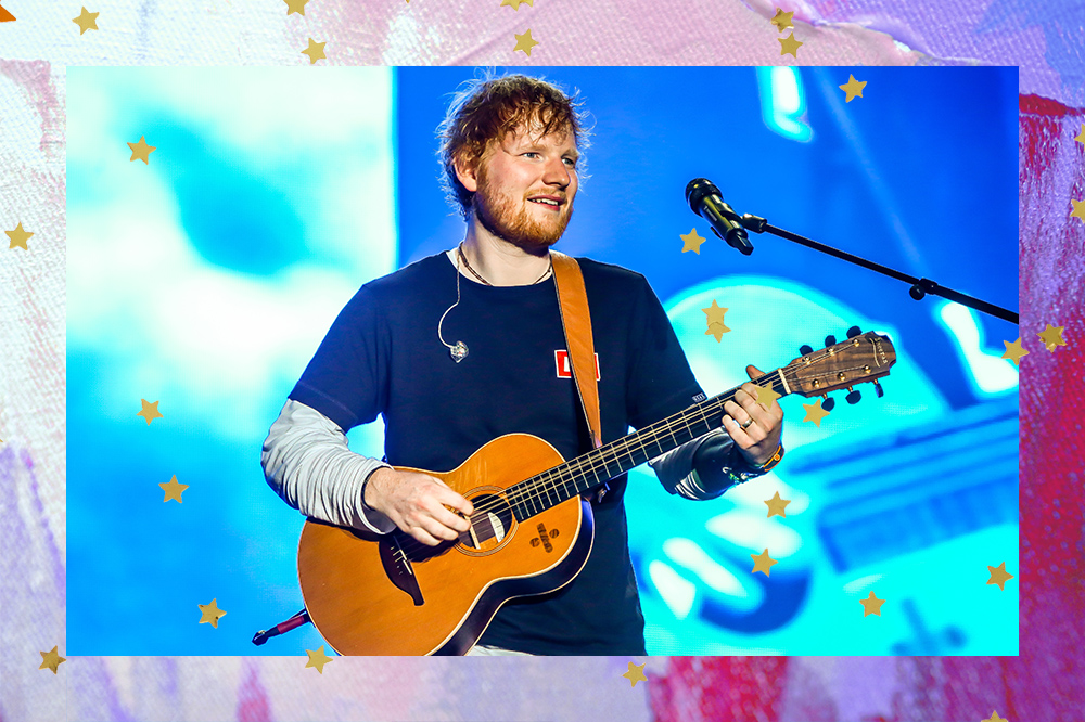 Ed Sheeran de cabelos ruivos e camisa preta, no palco com um violão na mão.
