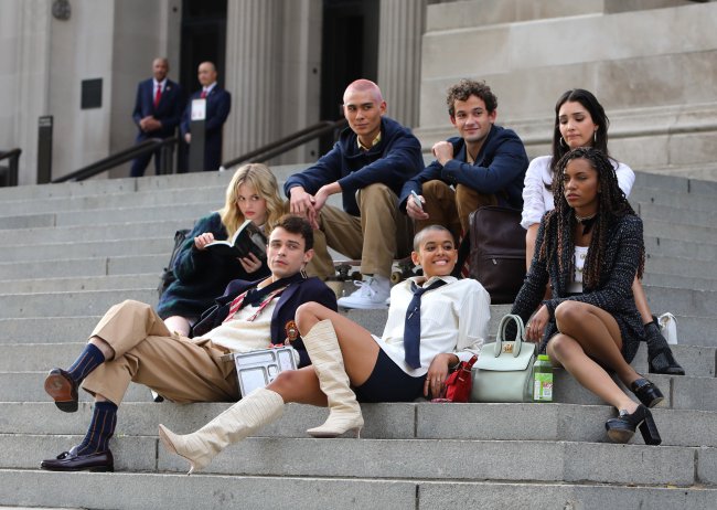 Elenco do reboot de Gossip Girl sentados na escadaria do MET, em Nova Iorque. Alguns atores estão olhando para tela ou sorrindo enquanto outros estão com expressões sérias