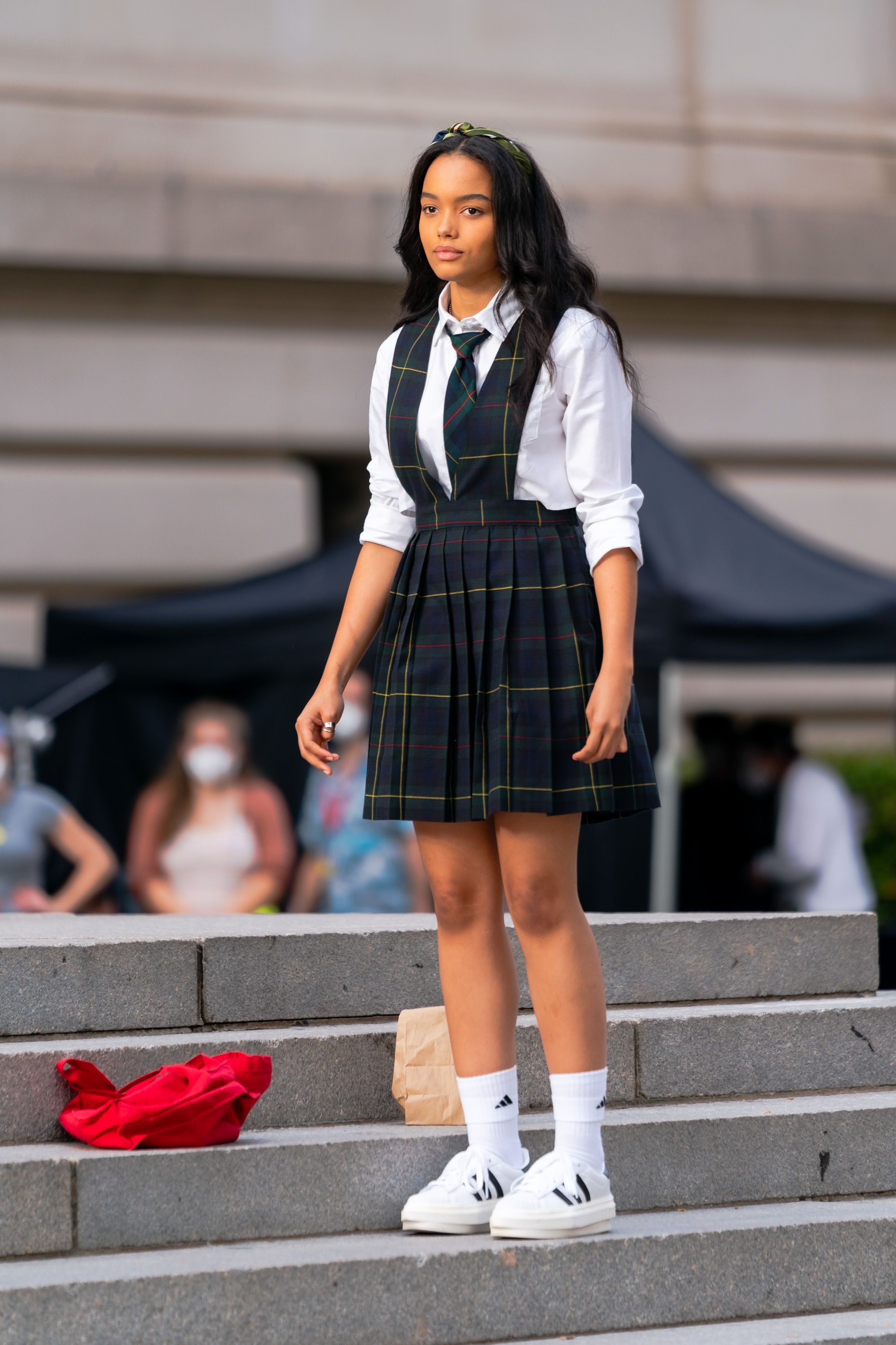 Reboot Gossip Girl Whitney Peak na gravação da nova versão de Gossip Girl. Ela está nas escadas do MET, em Nova York, usando camisa branca, gravata, salopete xadrez e tênis branco.