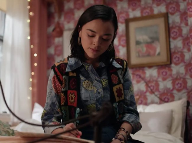 Foto da série Dash & Lily. Nela, aparece uma garota escrevendo em um caderno enquanto está sentada em sua cama. Ao fundo, seu quarto aparece com quadros e papel de parede estampado.