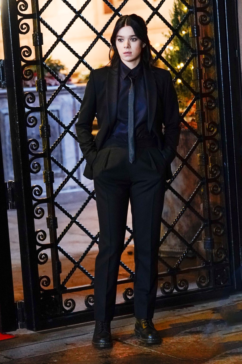 Hailee Steinfeld usando terninho preto formado por camisa, blazer, gravata e calça de alfaiataria com um coturno