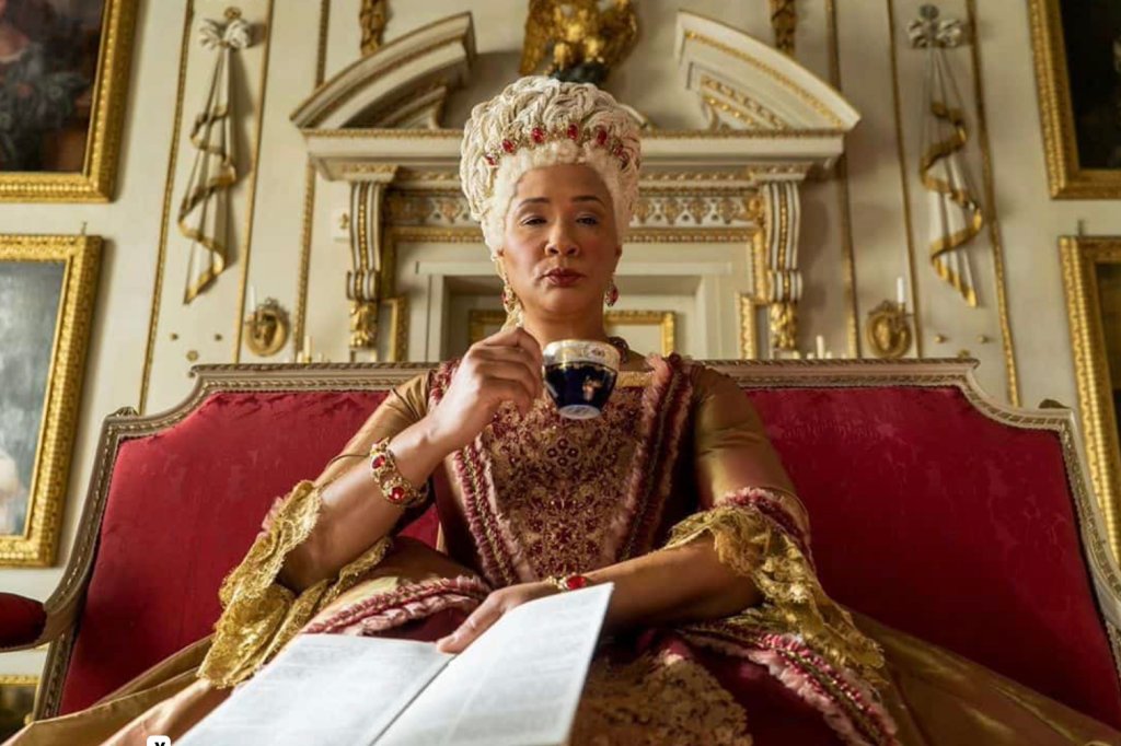 Rainha Charlotte em "Bridgerton" com uma xícara de chá na mão e um folhetim na outra.