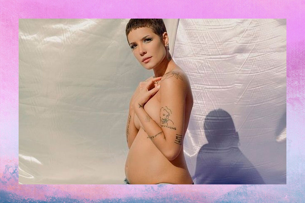 Halsey posando de perfil, sem blusa, com os braços cobrindo seu peito, mostrando a barriguinha de grávida