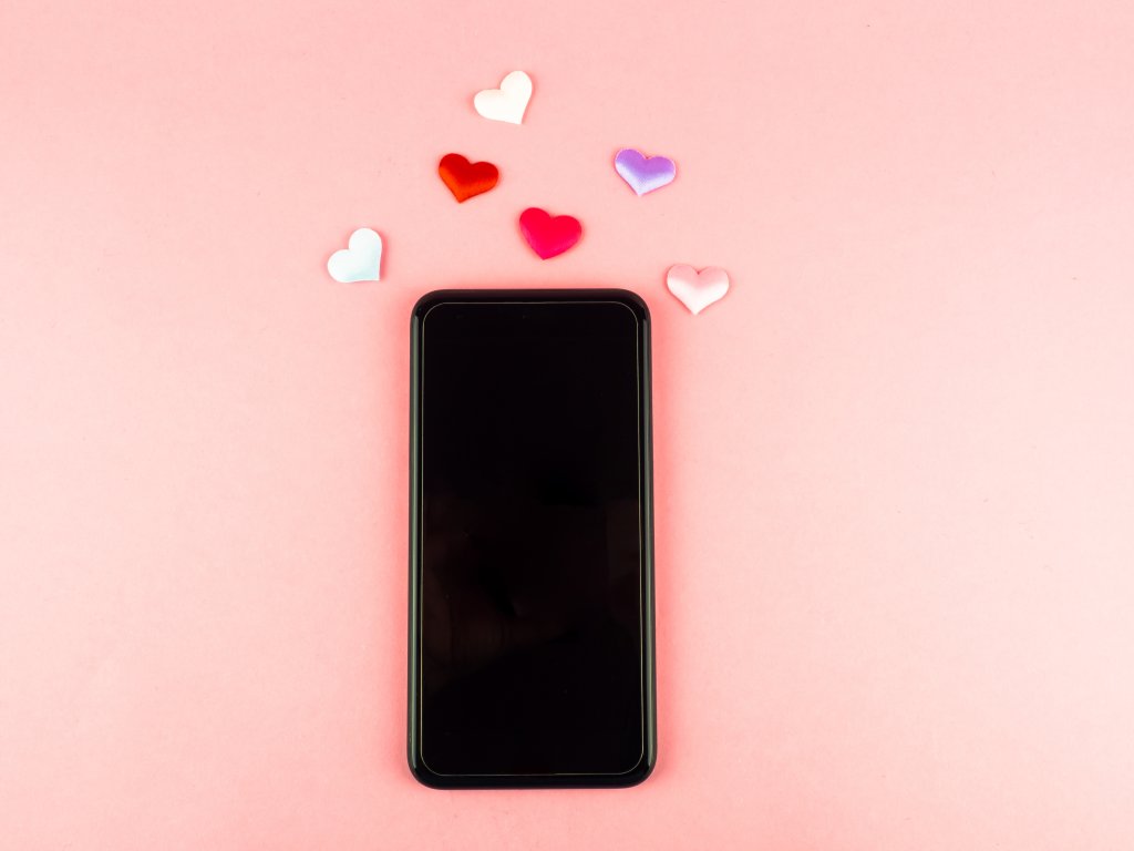 celular em fundo rosa com alguns corações próximos na parte de cima do aparelho