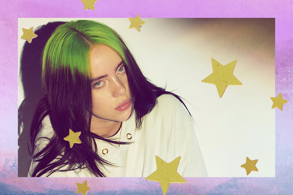 Billie Eilish posa com expressão séria. Ela olha para cima, em direção à câmera. A cantora usa um casaco branco e seu cabelo está solto, com raiz verde e o restante dos fios castanhos