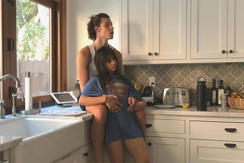 Shawn Mendes sentado na bancada da cozinha e Camila Cabello se apoiando nele