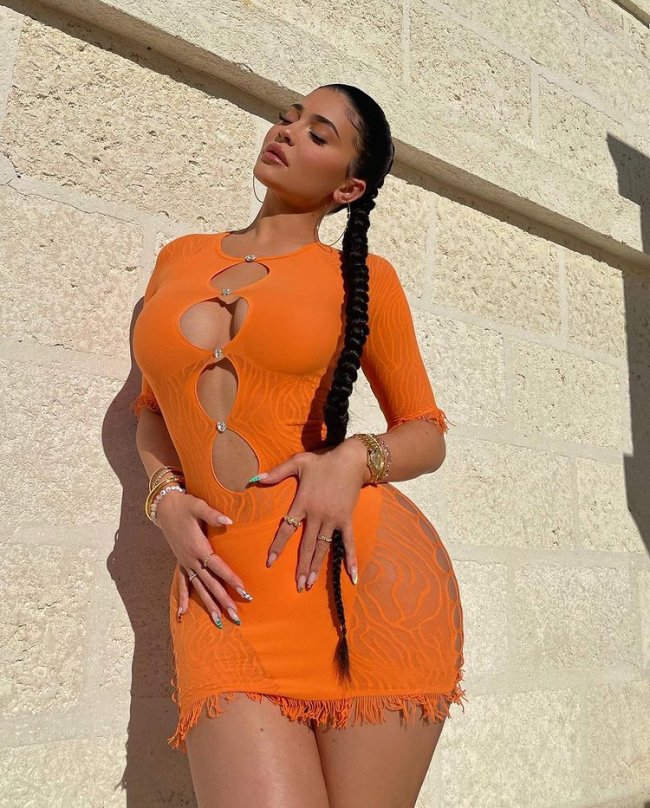Kylie Jenner usando vestido laranja com recortes circulares nas regiões do colo, dos seios e da barriga