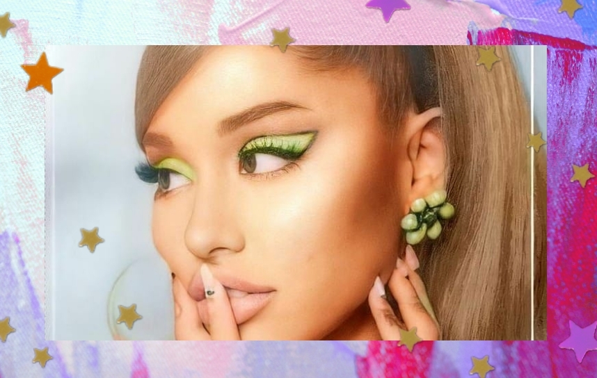 Ariana Grande olhando para o lado esquerdo, com as sobrancelhas levemente inclinada, usando tiara de cabelo preta, com brincos de flor verde, com as mãos no rosto, sendo uma delas em frente a boca. Ela usa uma blusa verde.