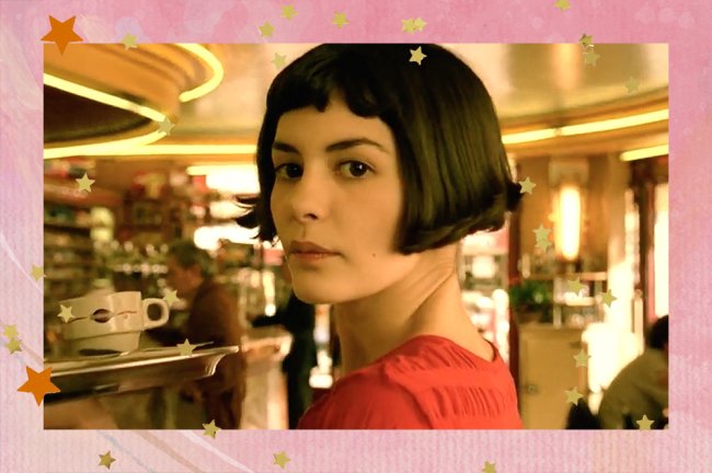 Amélie Poulain, interpretada por Audreu Tautou, aparece de cabelos curtos e camiseta vermelha. A personagem está no café em que trabalha e olha para o lado