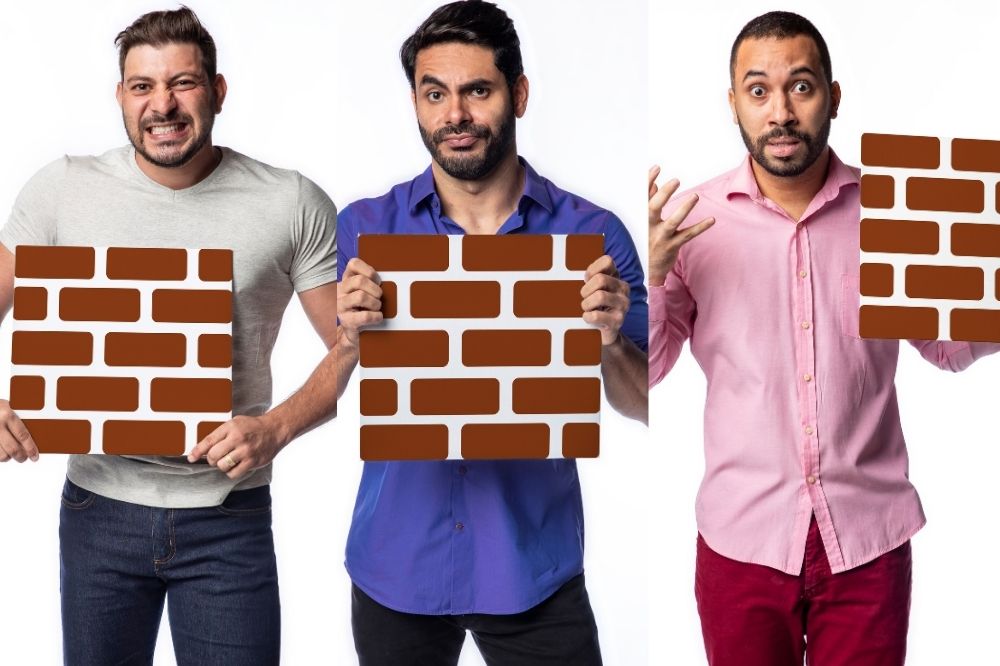 Caio, Rodolffo e Gilberto segurando parede de tijolos ilustrativa em imagem de divulgação do BBB21