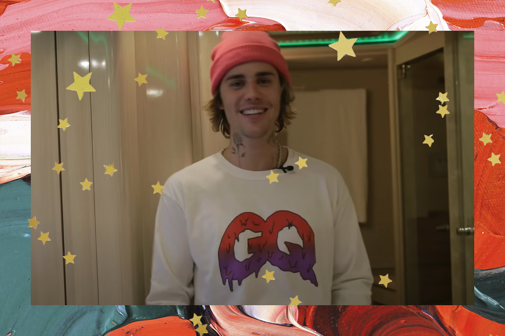 Justin Bieber usando camiseta branca e gorro vermelho, sorrindo dentro de seu ônibus de turnê