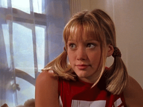 Gif da Hilary Duff na série Lizzie McGuire, nos anos 2000. Ela está fazendo uma expressão de sorriso "falso" enquanto gira a cabeça para o lado