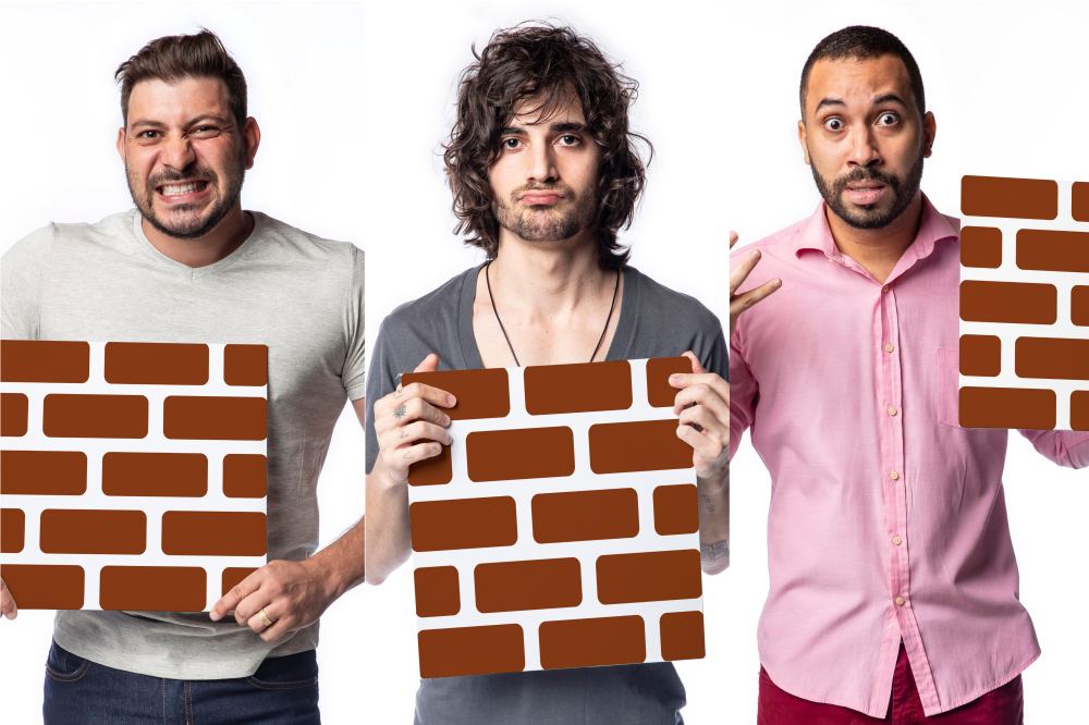 Montagem com os participantes do BBB21 Caio, Fiuk e Gilberto segurando uma peça que imita um muro de tijolos