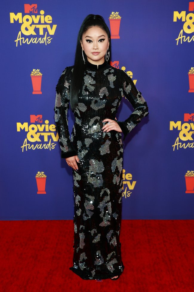 Atriz Lana Condor no MTV Movie & TV Awards Atriz Lana Condor no MTV Movie & TV Awards, usando vestido longo e preto com detalhes em prata, posando com uma mão na cintura e expressão sorridente no red carpet da premiação