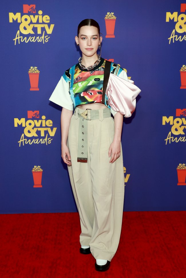 Atriz Victoria Pedretti no MTV Movie & TV Awards Atriz Victoria Pedretti no MTV Movie & TV Awards usando blusa verde com detalhes coloridos e manga bugante, calça bege, posando com os braços esticados ao lado do corpo e com expressão levemente sorridente.