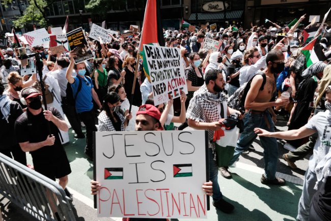 Manifestantes da causa palestina em rua de Nova York. Ela está lotada. Um deles segura um cartaz com os dizeres: 