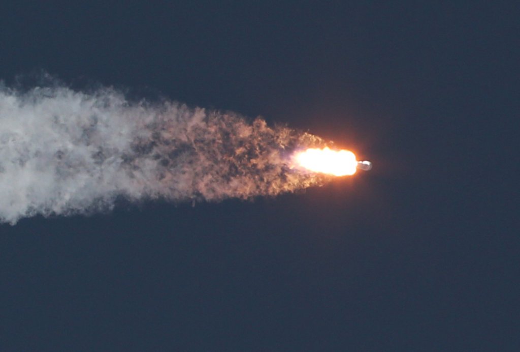 Imagem de um foguete sendo lançado; ele está voando na horizontal, liberando muito fogo e fumaça pela parte traseira; o céu está escuro