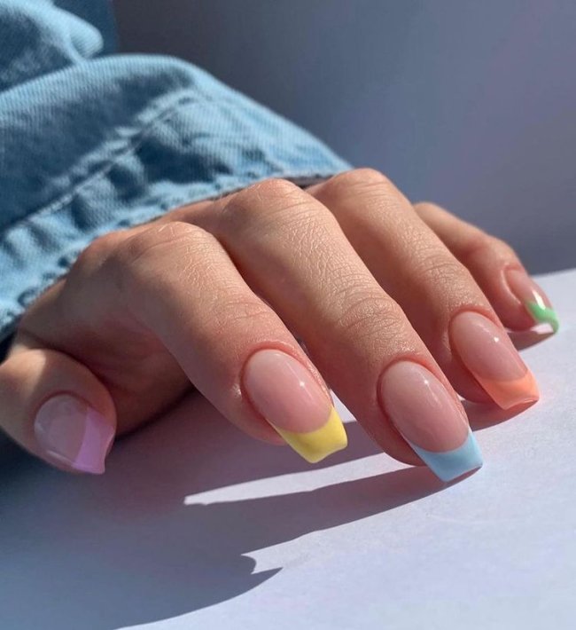 Foto mostrando uma mão com os dedos dobrados para evidenciar as unhas pintadas em francesinha colorida nas cores laranja, azul, rosa, verde e amarelo.