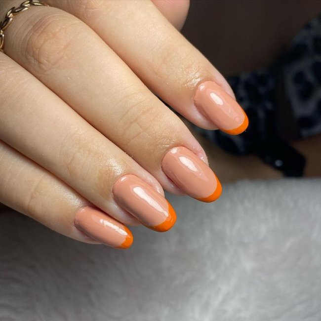 Foto mostrando uma mão com os dedos dobrados para evidenciar as unhas pintadas em francesinha colorida; com base laranja claro e francesinha com laranja escuro.